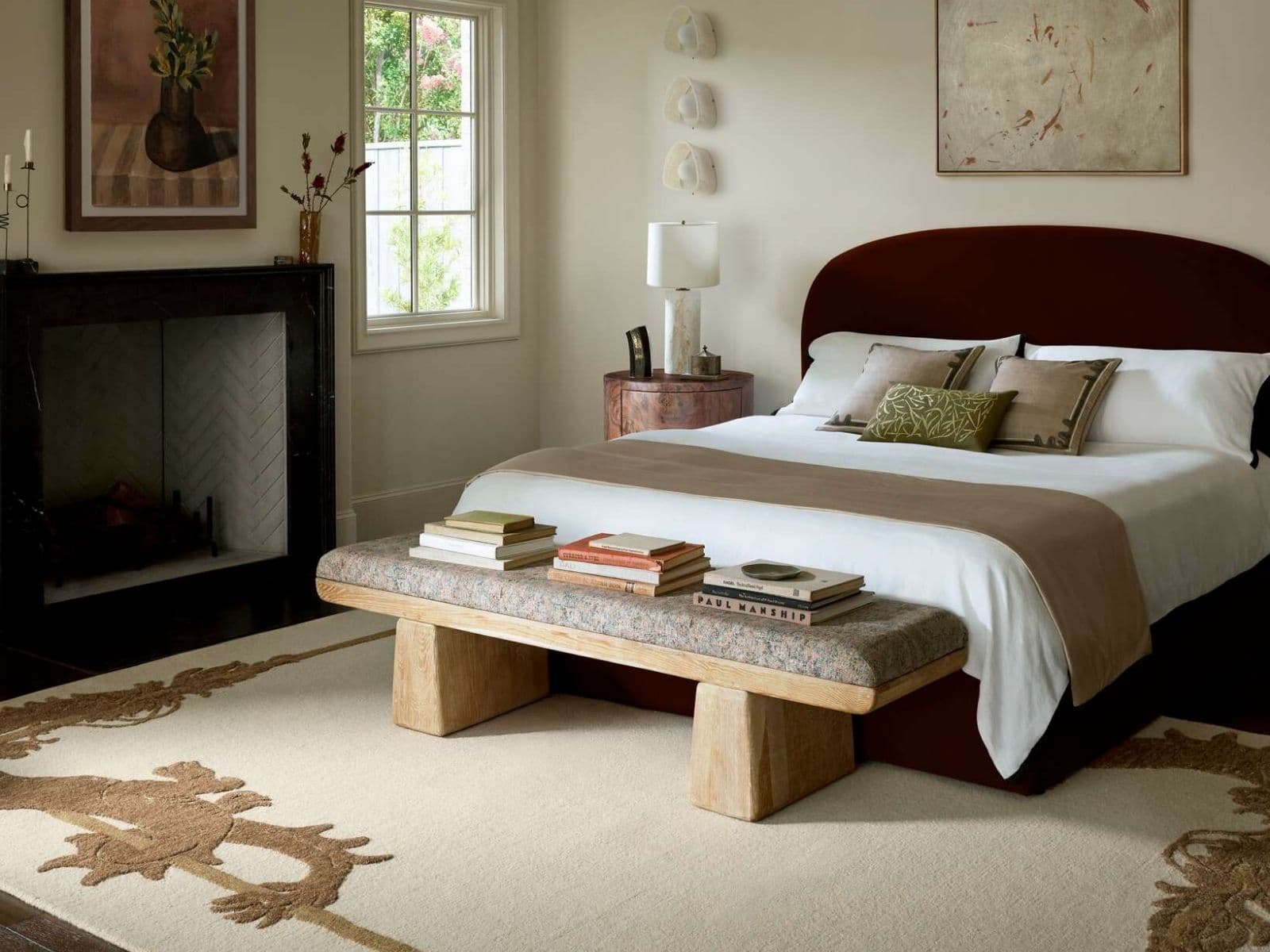 Bedroom with an oxblood arched headboard, oak bench and bordered wool rug